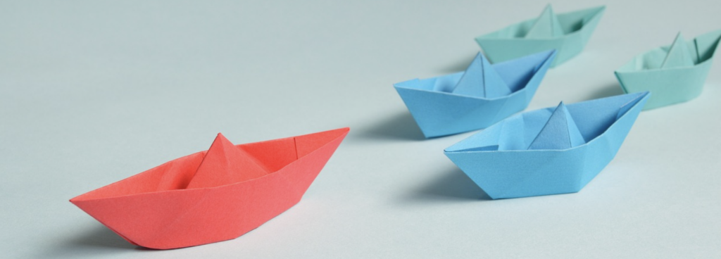 A set of paper boats with one larger red paper boat leading the others.